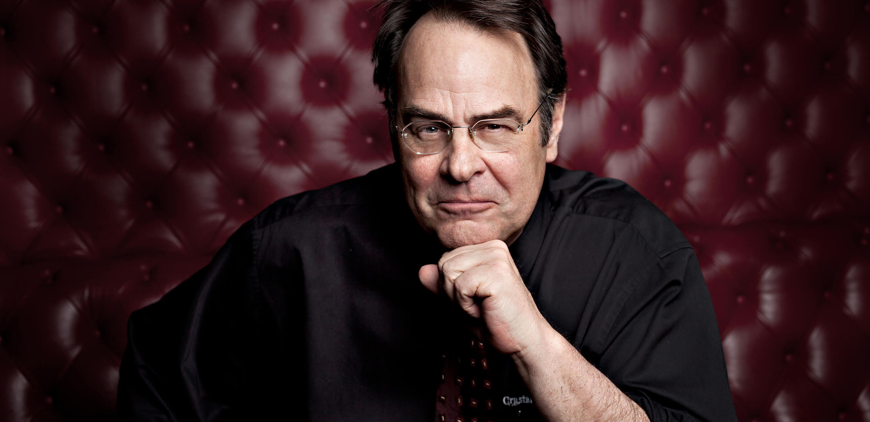 Dan Aykroyd poses for a headshot in a burgundy leather booth